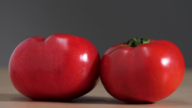 Hand lays a tomato on the table. Three ripe fresh juicy tomatoes lie on the table for a delicious salad. Red tomato on a gray background. Healthy vegetarian lifestyle concept. Close-up fresh vegetable