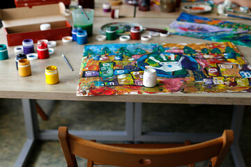 A bright watercolor drawing lies on a table next to cans with multi-colored paint. Art studio.