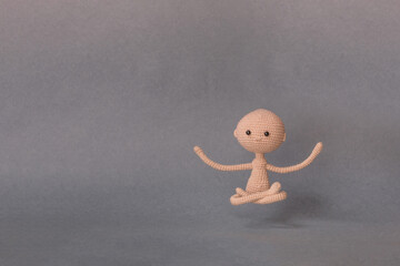 A toy man on a gray background with copy space. Cute amigurumi. Presentation PowerPoint or Keynote. Motivational phrase. Man sitting in Lotus position and levitating