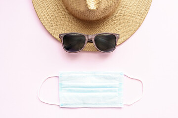 Ein Sonnenhut, eine Sonnenbrille und ein blauer Mundschutz auf einem rosa Hintergrund, Flat lay,...