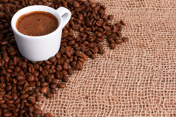 White cup of espresso and coffee beans on jute burlap sackcloth. Closeup, copy space. Coffee shop, morning, traditional roast concept