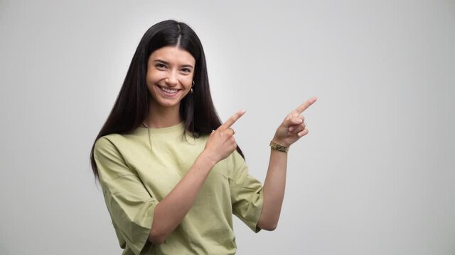 Young handsome caucasian girl indicates something with his hands. Isolated on grey background