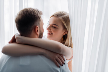 selective focus of smiling woman embracing and looking at boyfriend