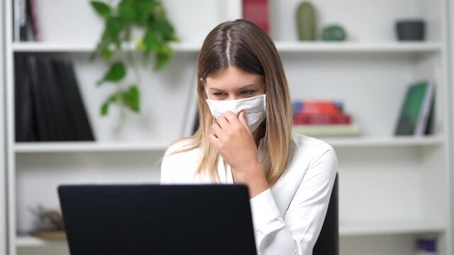 young girl works at the computer in her office and takes off her mask confident for the future