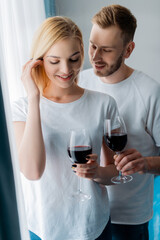handsome man looking at woman and holding glass with red wine