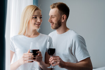 side view of happy man and cheerful woman holding glasses with red wine