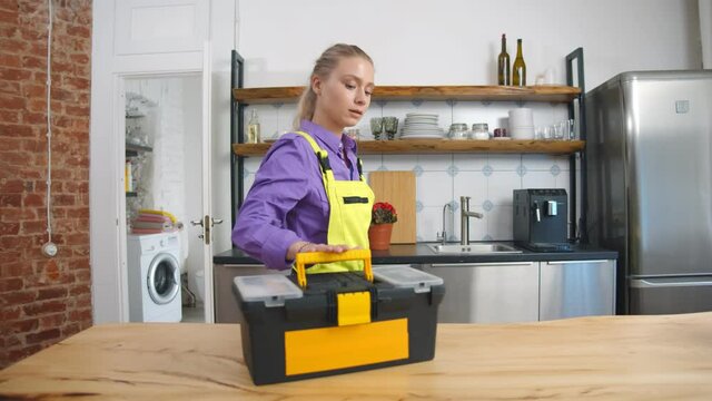 Pretty female plumber examining broken kitchen faucet