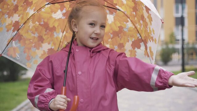 Pretty blond little girl with umbrella checking rain with palm. Portrait of cute Caucasian kid standing outdoors with hand stretched and smiling. Raining season, lifestyle, childhood, leisure.