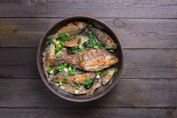 Frying pan with tasty crucian carp on wooden background 