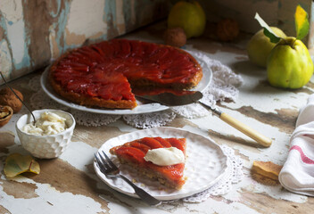 Quince tarte tatin served with whipped cream, quince fruits and walnuts on a wooden surface. Rustic style.