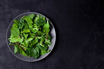 Green salad with spinach on black background, top view