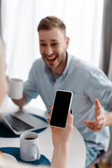 selective focus of girl holding smartphone with blank screen near cheerful freelancer boyfriend