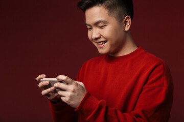 Image of joyful young asian man smiling and using mobile phone