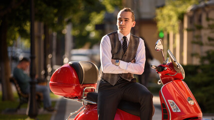 Portrait of young handsome man in classic vest and white shirt on a red vintage motorbike scooter