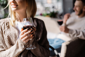 cropped view of happy girl holding glass with red wine near man