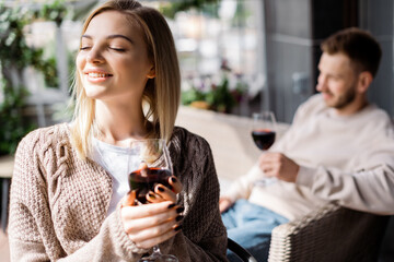 selective focus of cheerful girl with closed eyes holding glass of red wine near man