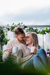 selective focus of happy man and smiling woman holding cups of tea and sitting on outdoor sofa