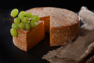 A large head of hard cheese on a black background. A triangular piece of cheese with grapes. Out of focus. Copy of the space.Photo on a black background.Top view.