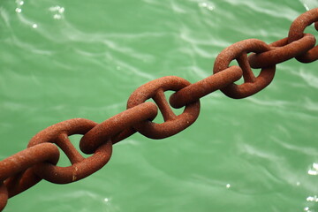Rusty mooring chain links over green sea water