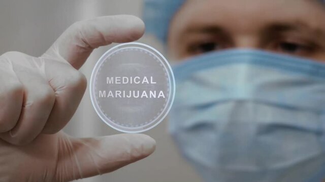 Doctor looks at innovative holographic projection with text Medical Marijuana. Male scientist in medical mask conducting technological research on hologram. Concept of futuristic medicine