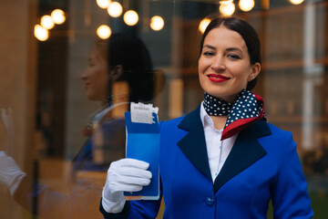 Obraz premium Closeup face of smiling flight attendant, female airline employee holding boarding pass with passenger's passport