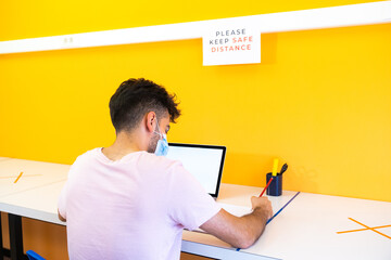 Young student boy doing his homework at school with the computer in the new normal. Back to school concept. Please maintain a safe distance.