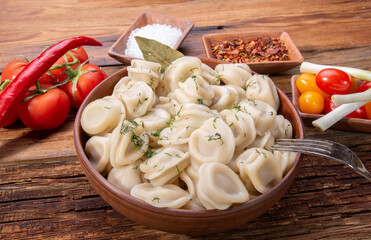 homemade meat dumplings on a wooden antique table with fresh tomatoes, onions and spices, top view