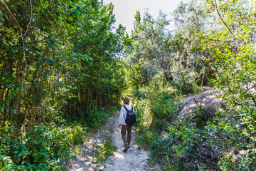 Obraz premium Young adventurer boy with backpack and hat walks through the interior of a Mediterranean forest in Spain. Selective focus.