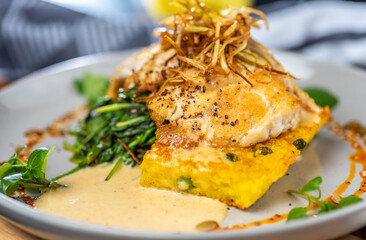 A serve of grilled Barramundi fish with Paella Risotto cake, presented on a round plate