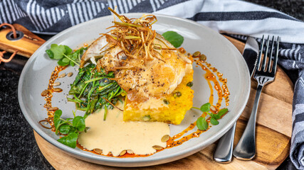 A serve of grilled Barramundi fish with Paella Risotto cake, presented on a round plate