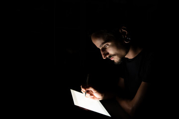 Face of a man illuminated by a tablet screen while using a digital pen