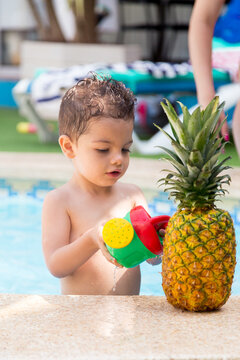 Child inside a pool playing with a toy next to a pineapple