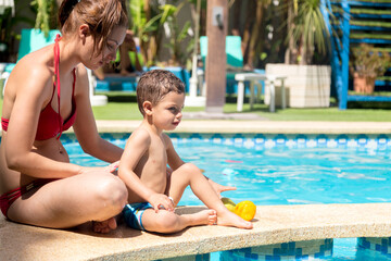 Mother and child sitting at the edge of a pool with different pieces of fruit