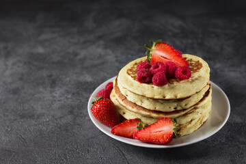 Homemade pancakes with raspberries and strawberries on a dark background.