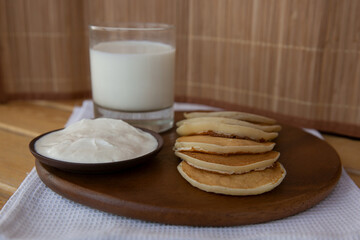 pancakes with sour cream and a glass of milk on a wooden base