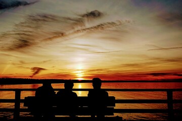 Drei Silhouetten auf eine Bank vor Sonnenuntergang.