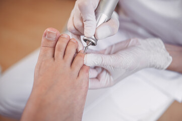 Obraz na płótnie Canvas Hardware medical pedicure with nail file drill apparatus. Patient on pedicure treatment with pediatrician chiropodist. Foot peeling treatment at spa with a special device. Clinic of Podiatry Podology