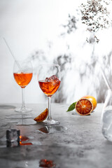 Refreshing aperol spritz cocktail with straw and sliced orange on a grey background- summer day sunlight shadows