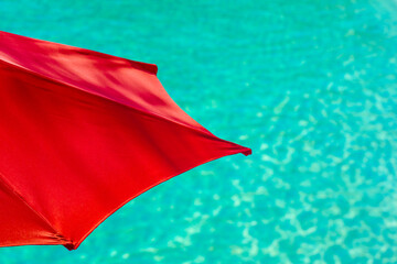 Vibrant Summer Vacation Travel Background With Red Parasol and Teal Water © ystewarthenderson