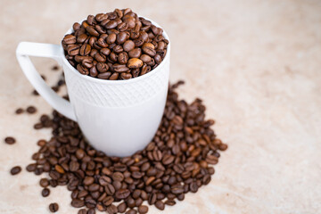 a white cup filled with roasted cinnamon coffee beans standing on brown marble surrounded by coffee beans