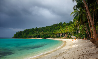 Tropical beach before the storm. The sun shines on the white sand against the background of storm...