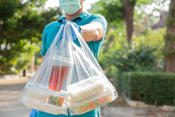  Food boxes in plastic bags delivered to customer at home by delivery man wearing face mask and wear hygiene gloves in green shirt.delivery service during covid19