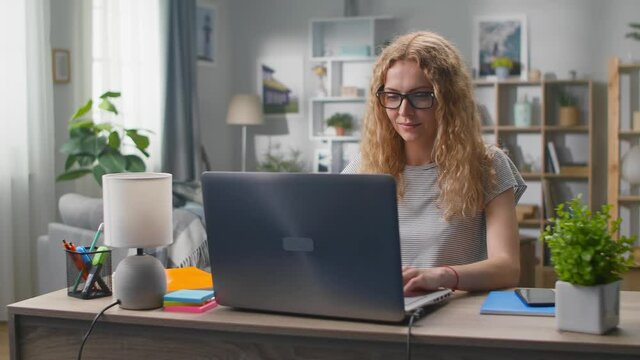 Young woman with laptop at the desk ooking at the camera