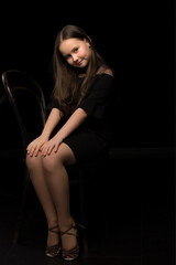 Portrait of a little girl sitting on an old Viennese chair, black background.