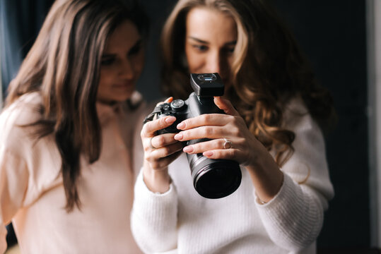 Women model and female photographer watching photos in studio. Concept of creative work in photo studio, backstage job.