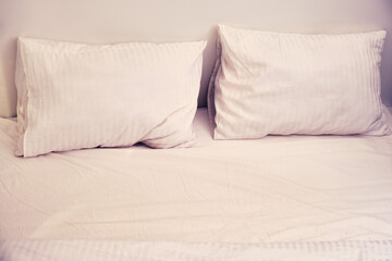 Two pillows on an empty white bed in the evening