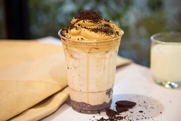 Close up a cup of Dalgona coffee with a cookies crumb on a white table with a cup of milk at night.