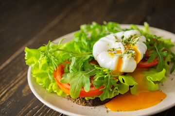 Light breakfast, poached egg with salad, tomatoes and arugula on dark bread
