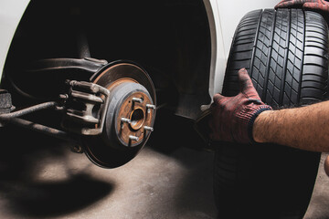 The mechanic's hand holding black tires for changing alloy wheel into the wheel hub at car tire...