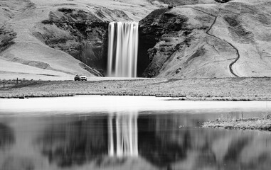 Car parked in front of a waterfall in Iceland. The reflection of both completes the look.